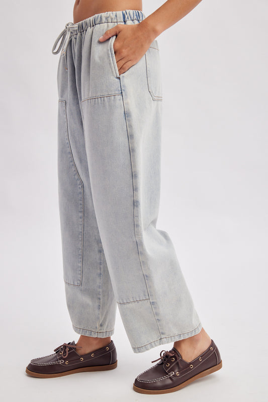 A women's light wash drawstring barrel-leg denim jeans featuring an elastic tie waistband, deep front patch pockets, and curved leg paneling.