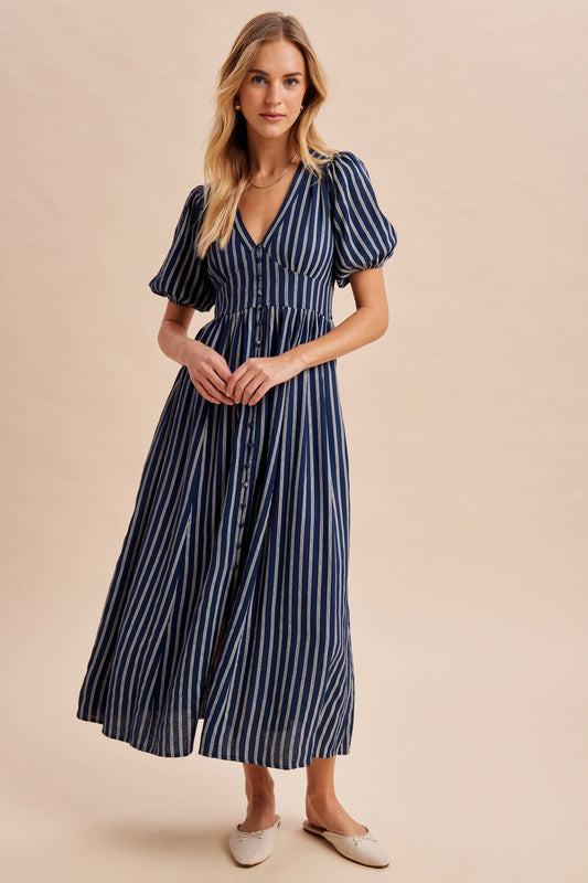 A women's navy blue and cream vertically striped short puff sleeve maxi dress featuring a V-neckline, full front button placket, and high gathered waistline.