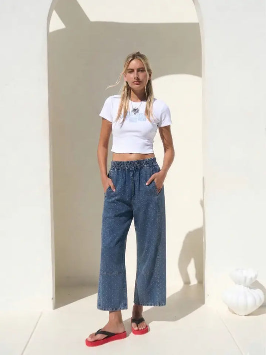 High-waisted wide-leg denim pants featuring an all-over white micro polka dot print, a comfortable smocked elastic waistband, and functional side pockets.