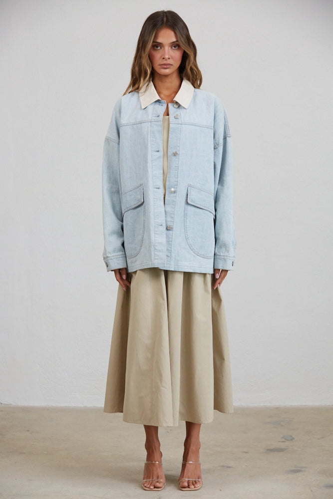 A women's relaxed oversized light wash denim utility jacket featuring a cream-colored pointed contrast collar, a button-front closure, and large front patch pockets with flaps.