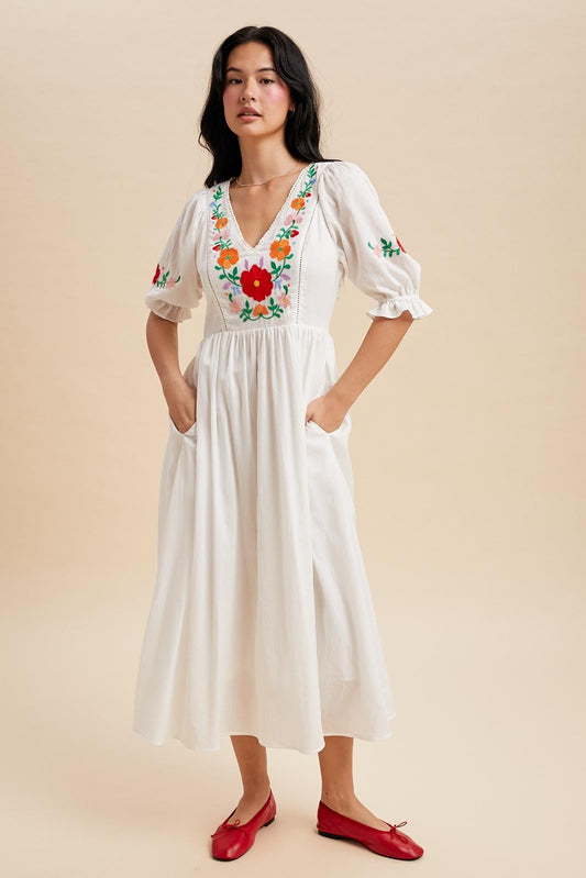 Off white maxi dress with a v-neck and embroidered bodice. The sleeves are cuffed with a ruffle detail and hit just above the elbow with minimal embroidered detail.