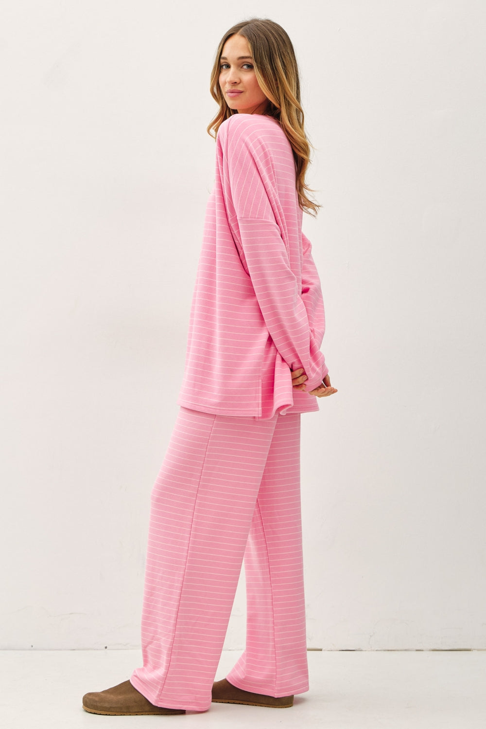 A women's relaxed long-sleeve crewneck top in bubblegum pink with ivory horizontal micro-stripes, dropped shoulders, and subtle side hem vents.