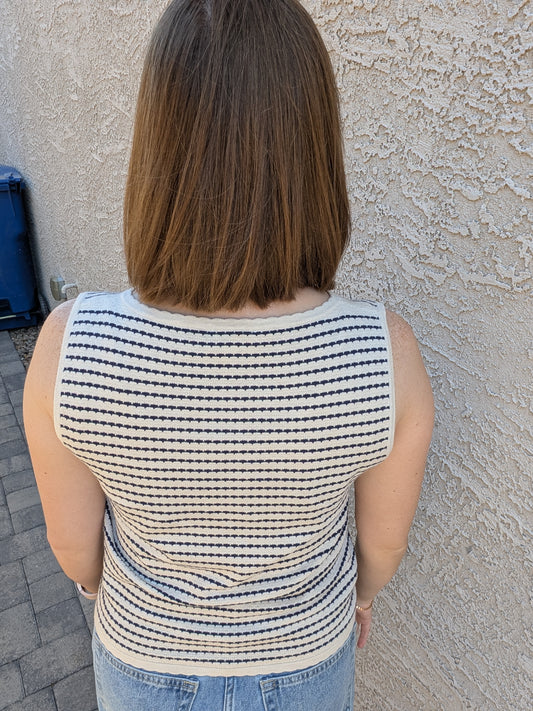 A sleeveless horizontal stripe knit sweater tank featuring a high boatneck, delicate ribbed trim at the hem and armholes, and a neutral oatmeal and navy color palette.