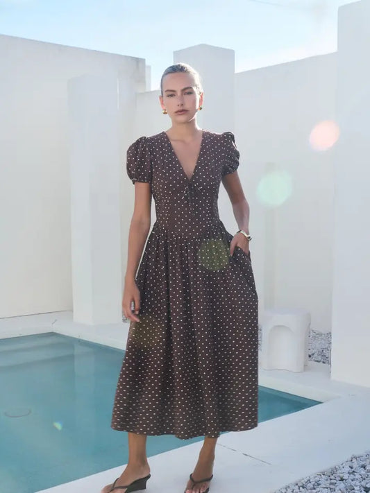 A short-sleeve brown and white polka dot midi dress featuring a V-neckline with a keyhole front tie detail, structured puff sleeves, and functional side pockets.