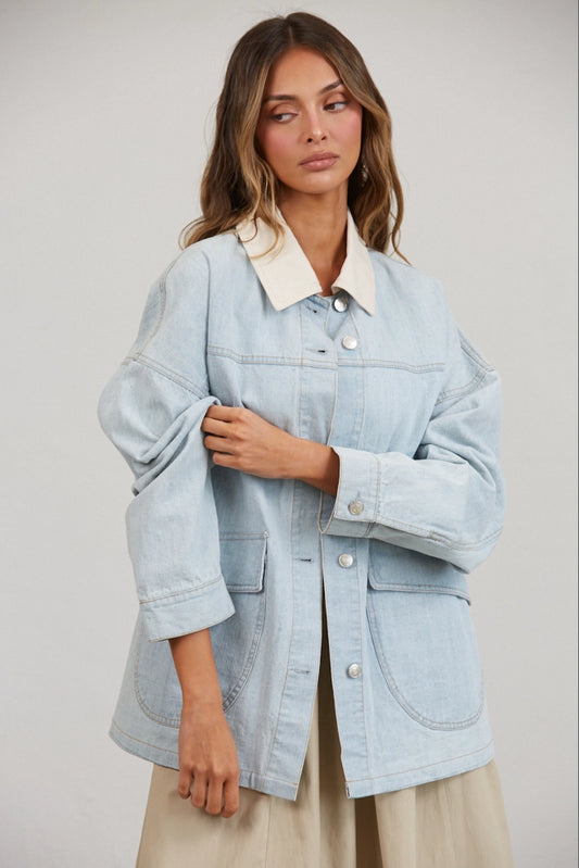 A women's relaxed oversized light wash denim utility jacket featuring a cream-colored pointed contrast collar, a button-front closure, and large front patch pockets with flaps.
