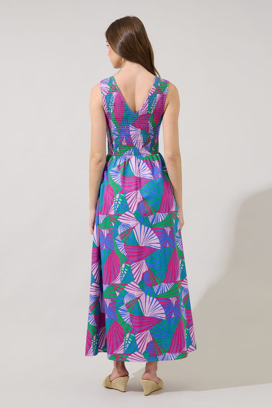 A sleeveless midi dress in a vibrant pink and blue tropical fan print featuring a stretchy smocked bodice, a V-neckline, and functional side pockets.