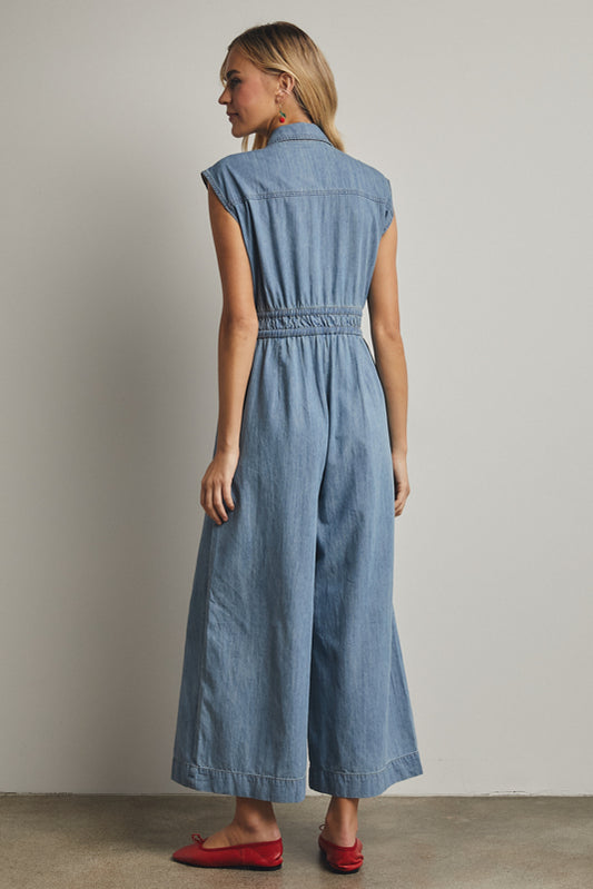 A cap-sleeve light wash denim jumpsuit featuring a classic button-down front, an adjustable drawstring waist, and a relaxed wide-leg fit.