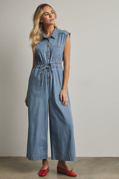 A cap-sleeve light wash denim jumpsuit featuring a classic button-down front, an adjustable drawstring waist, and a relaxed wide-leg fit.
