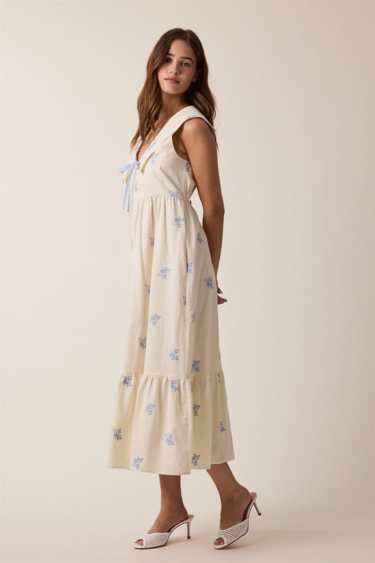 Cream sleeveless midi dress with floral design. A slight hooded peter-pan collar and a front blue accent tie. Featuring side pockets. 