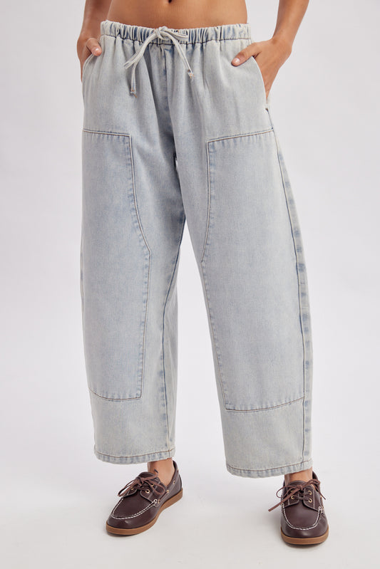 A women's light wash drawstring barrel-leg denim jeans featuring an elastic tie waistband, deep front patch pockets, and curved leg paneling.