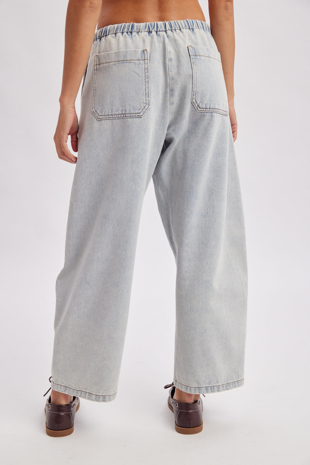A women's light wash drawstring barrel-leg denim jeans featuring an elastic tie waistband, deep front patch pockets, and curved leg paneling.