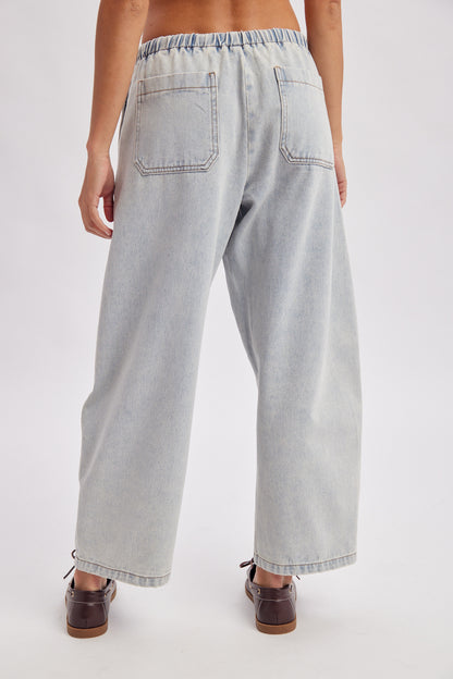 A women's light wash drawstring barrel-leg denim jeans featuring an elastic tie waistband, deep front patch pockets, and curved leg paneling.