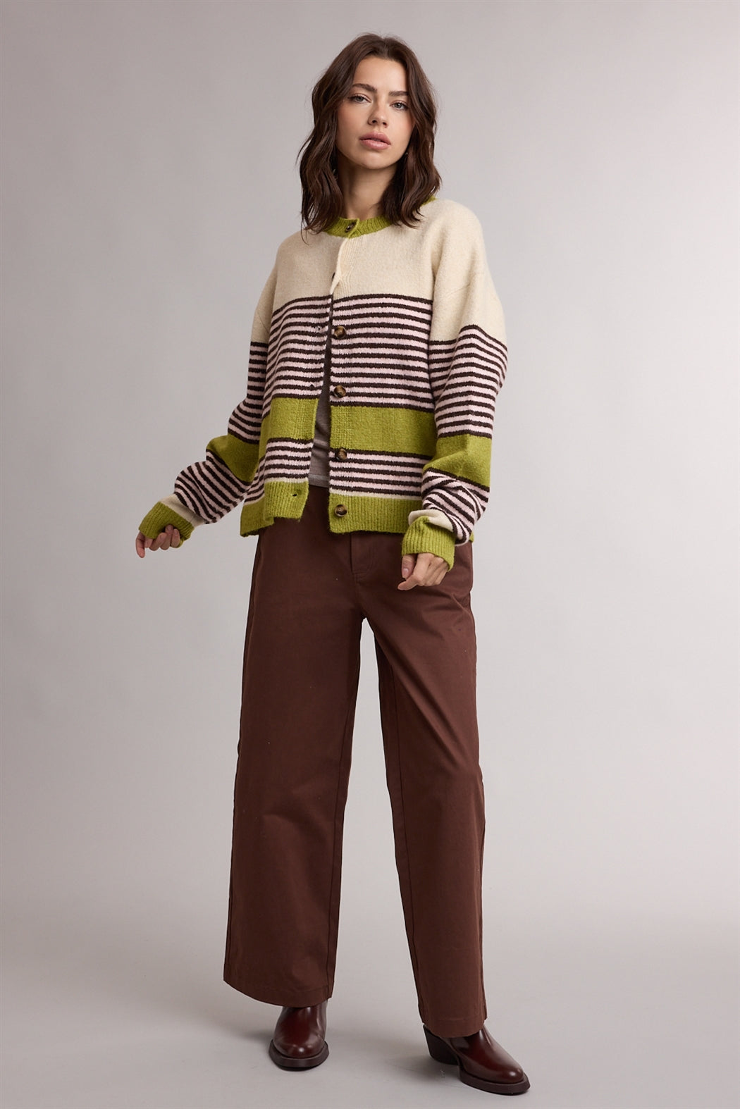 A women's relaxed crewneck knit cardigan featuring wide avocado green colorblocking and horizontal espresso stripes on a cream background with tortoiseshell-look front buttons.