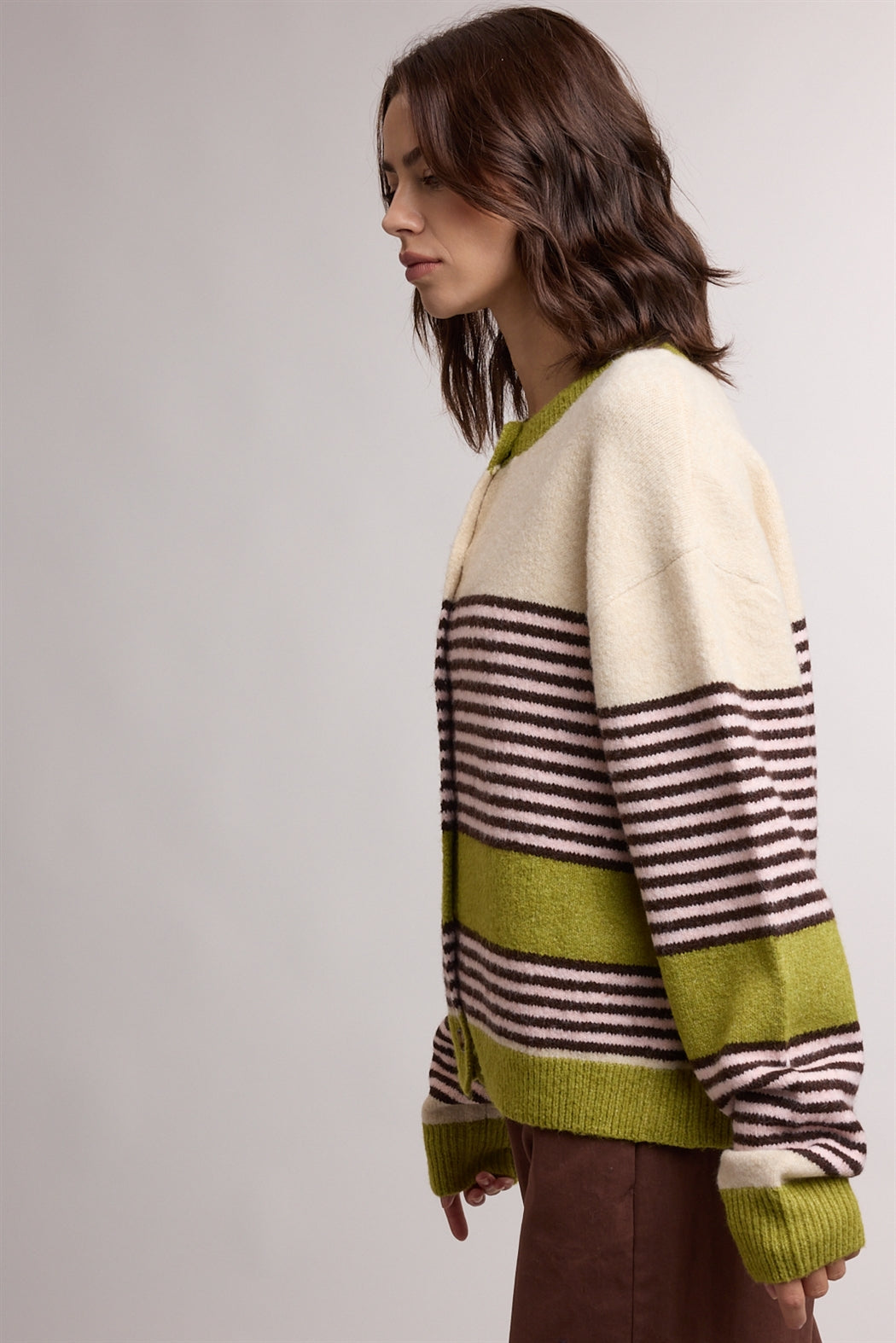A women's relaxed crewneck knit cardigan featuring wide avocado green colorblocking and horizontal espresso stripes on a cream background with tortoiseshell-look front buttons.