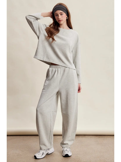 A women's heather gray two-piece stretch cotton lounge set featuring a long-sleeve crewneck top and matching high-waisted relaxed wide-leg pants.