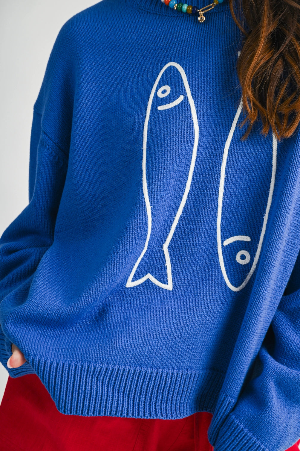 A women's royal blue long-sleeve knit crewneck sweater featuring a white embroidered sardine graphic on the front and ribbed trim along the collar, cuffs, and hem.