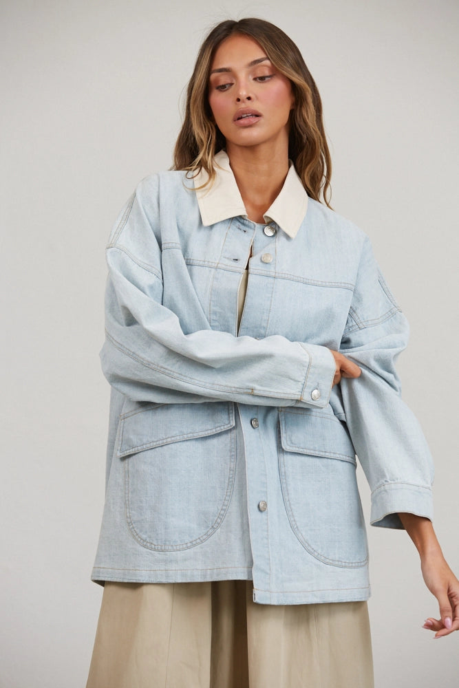 A women's relaxed oversized light wash denim utility jacket featuring a cream-colored pointed contrast collar, a button-front closure, and large front patch pockets with flaps.