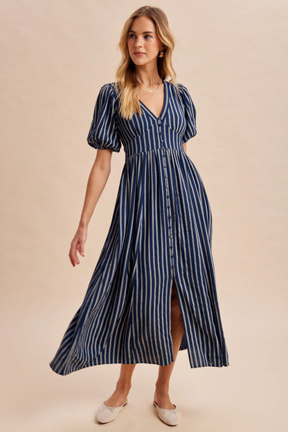 A women's navy blue and cream vertically striped short puff sleeve maxi dress featuring a V-neckline, full front button placket, and high gathered waistline.
