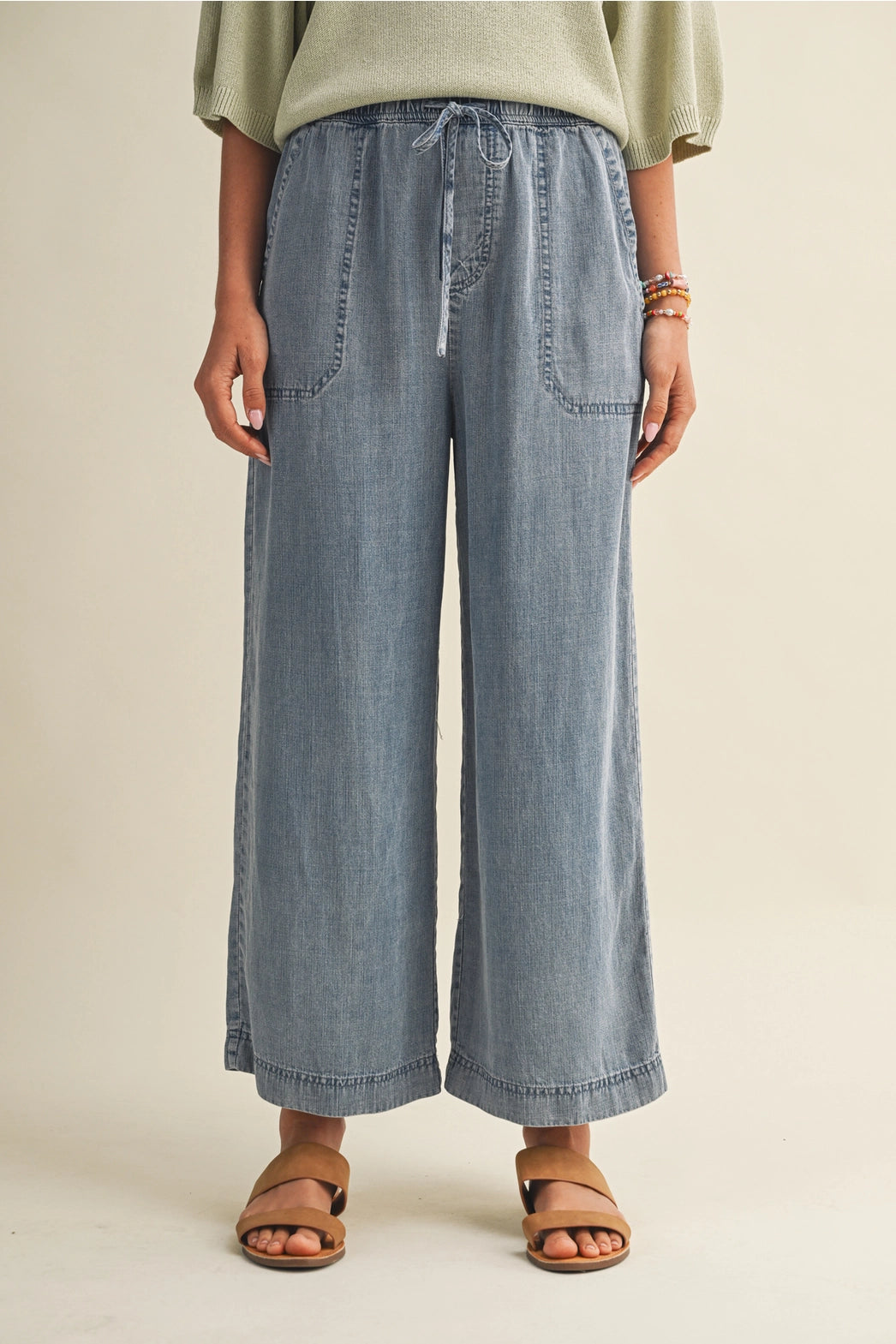 A pair of women's high-waisted wide-leg denim chambray pants featuring a gathered elastic drawstring waistband and functional front patch pockets.