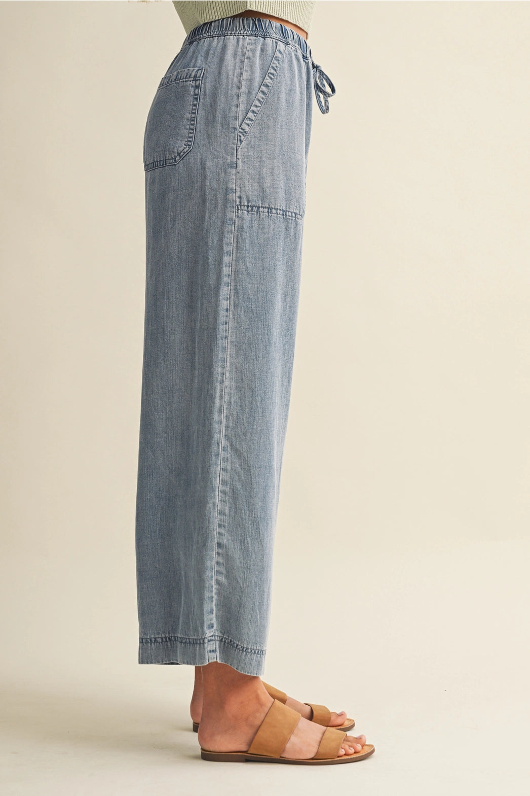A pair of women's high-waisted wide-leg denim chambray pants featuring a gathered elastic drawstring waistband and functional front patch pockets.