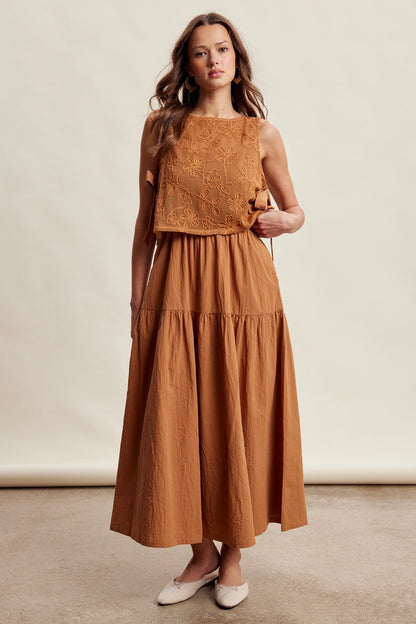 A women's brown sleeveless tiered maxi dress featuring a tonal embroidered floral lace vest overlay with adjustable side tie details.