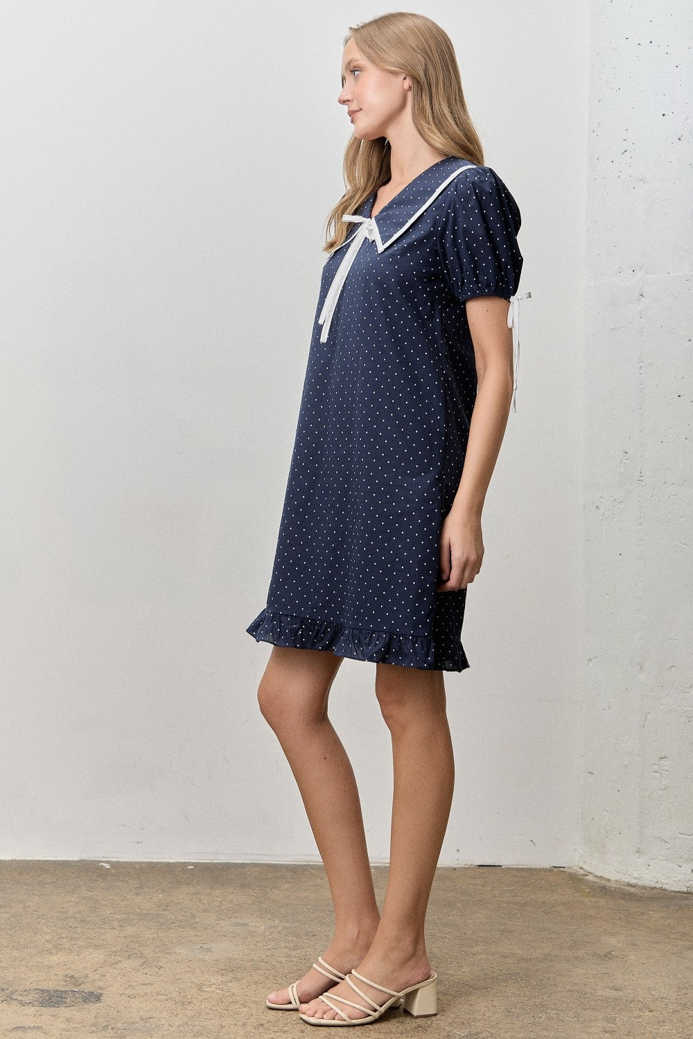 Just above the knee navy dress with white polka dots. 
V-neck with a peter pan collar and a ribbon tie. 
Minimally puffed sleeves with ribbon ties
Ruffled hem 