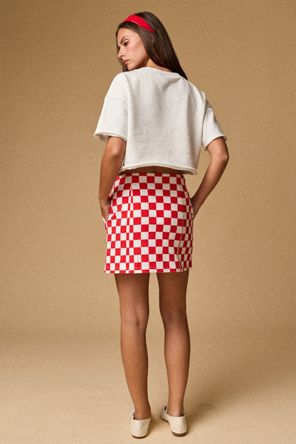 A women's light gray short-sleeve graphic t-shirt featuring a relaxed fit, a raw cut cropped hemline, and a textured patchwork American flag design made from blue star print, red gingham, and white eyelet lace fabrics.