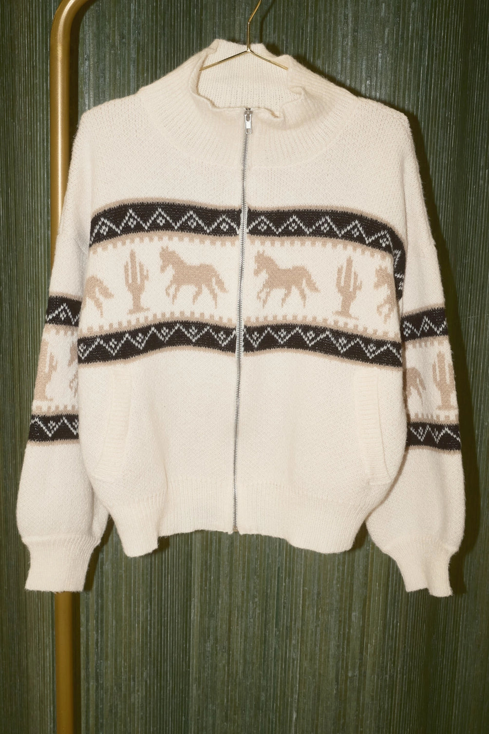 A women's cream knit zip-up collared sweater jacket featuring a southwestern geometric pattern, tan galloping horse motif, high collar, and front slip pockets.