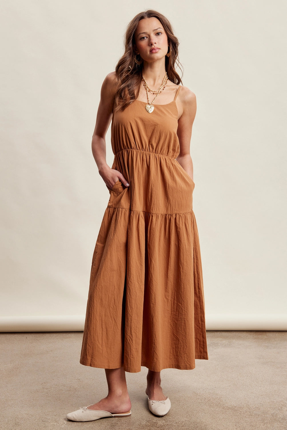 A women's brown sleeveless tiered maxi dress featuring a tonal embroidered floral lace vest overlay with adjustable side tie details.