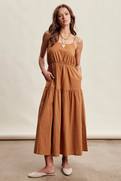 A women's brown sleeveless tiered maxi dress featuring a tonal embroidered floral lace vest overlay with adjustable side tie details.