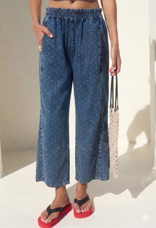 High-waisted wide-leg denim pants featuring an all-over white micro polka dot print, a comfortable smocked elastic waistband, and functional side pockets.