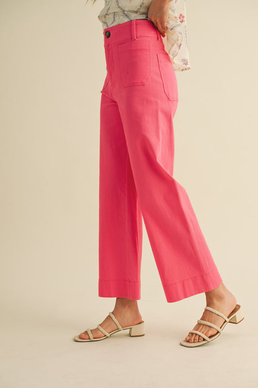 A pair of women's high-waisted wide-leg cropped cotton twill pants in a vibrant berry pink color featuring classic front patch pockets and a button zip closure.