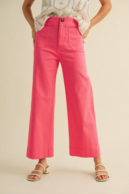 A pair of women's high-waisted wide-leg cropped cotton twill pants in a vibrant berry pink color featuring classic front patch pockets and a button zip closure.