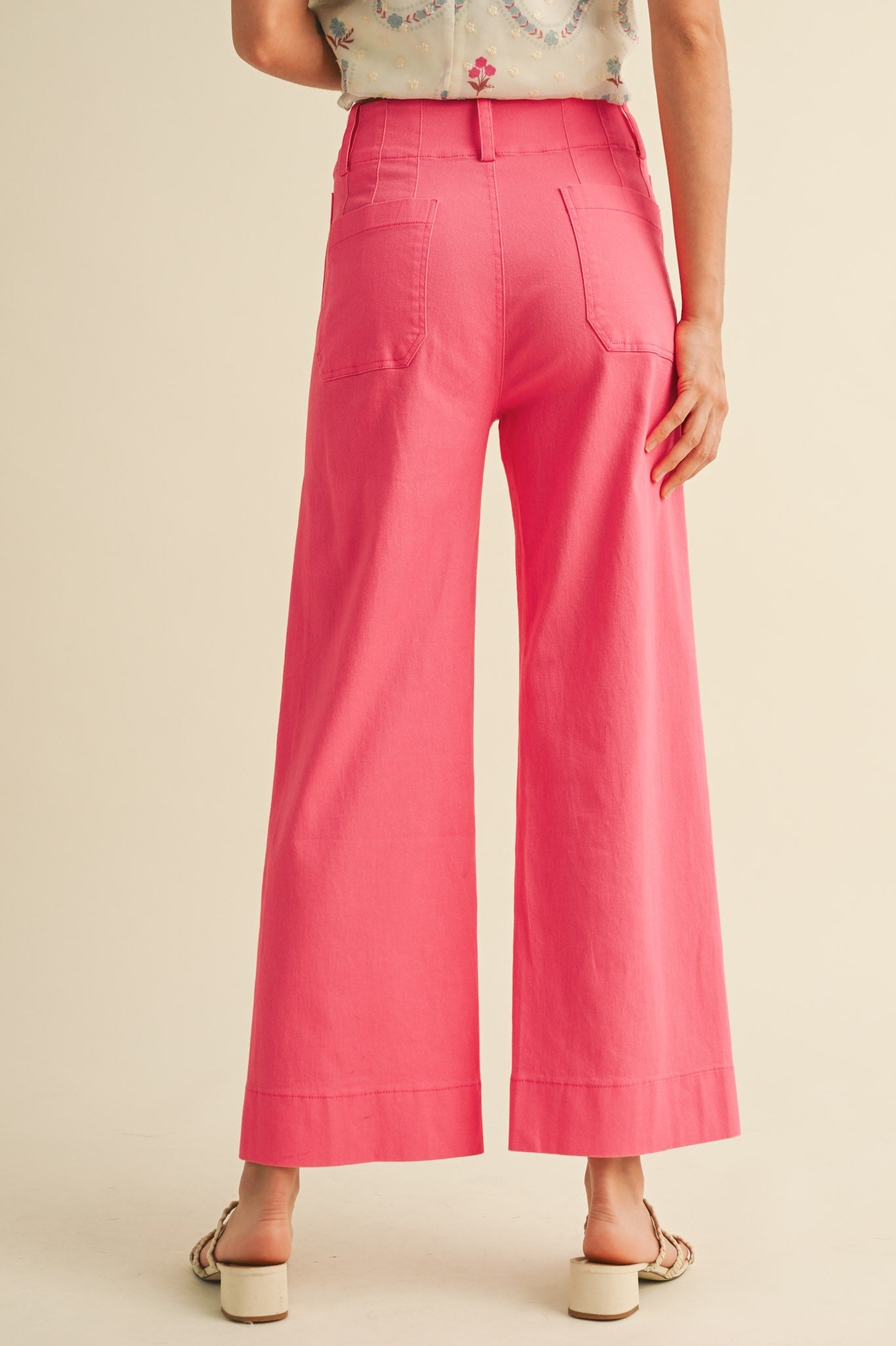 A pair of women's high-waisted wide-leg cropped cotton twill pants in a vibrant berry pink color featuring classic front patch pockets and a button zip closure.