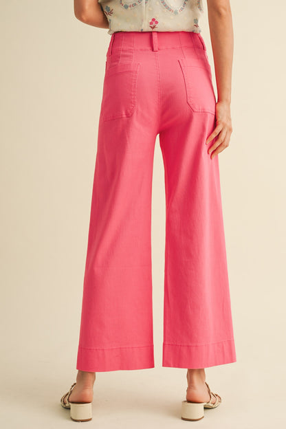 A pair of women's high-waisted wide-leg cropped cotton twill pants in a vibrant berry pink color featuring classic front patch pockets and a button zip closure.
