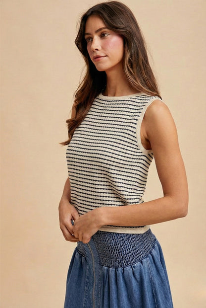 A sleeveless horizontal stripe knit sweater tank featuring a high boatneck, delicate ribbed trim at the hem and armholes, and a neutral oatmeal and navy color palette.