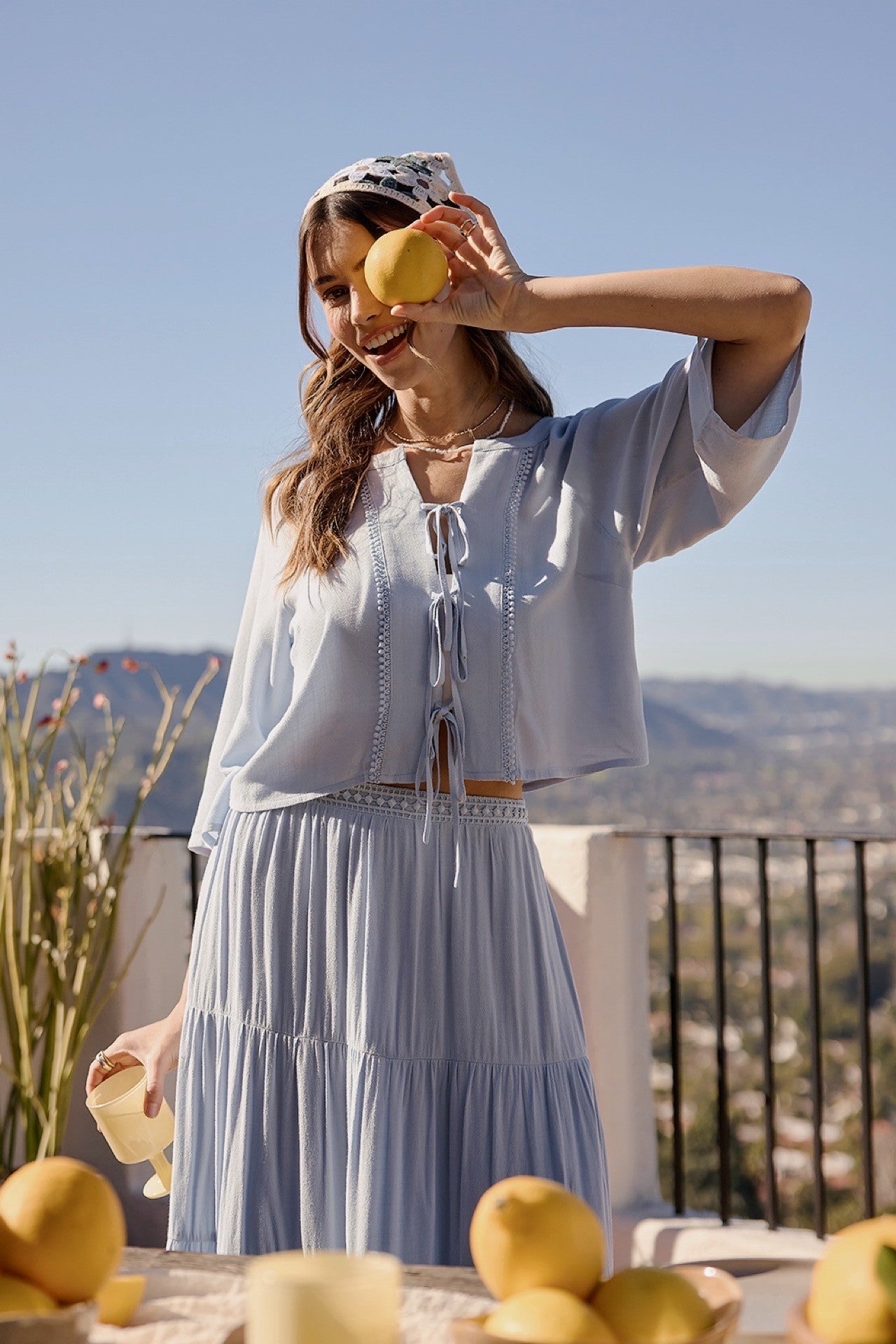 A two-piece sky blue set featuring a tie-front blouse with delicate lace trim details and short flowy sleeves paired with a matching tiered midi skirt.