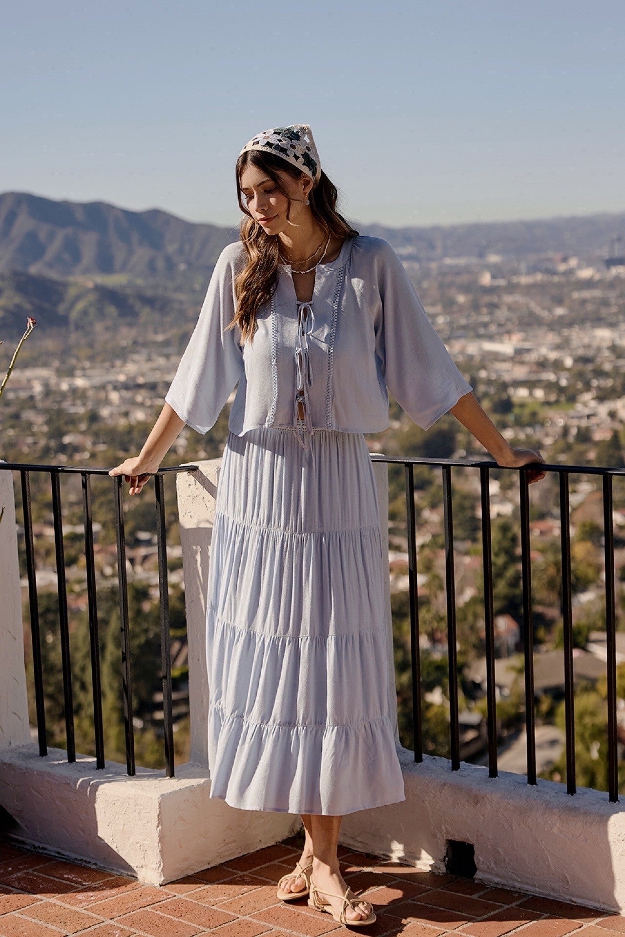 A two-piece sky blue set featuring a tie-front blouse with delicate lace trim details and short flowy sleeves paired with a matching tiered midi skirt.