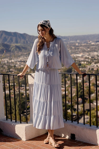 A two-piece sky blue set featuring a tie-front blouse with delicate lace trim details and short flowy sleeves paired with a matching tiered midi skirt.