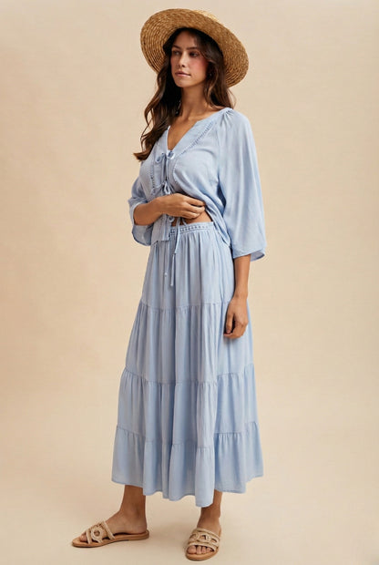A two-piece sky blue set featuring a tie-front blouse with delicate lace trim details and short flowy sleeves paired with a matching tiered midi skirt.
