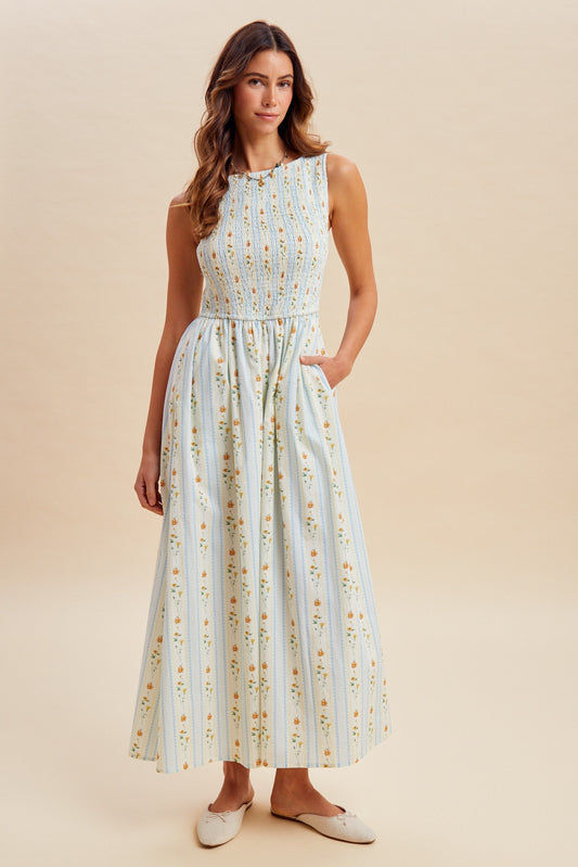 A sleeveless women's high-neck midi dress featuring a fully smocked bodice, convenient side pockets, and an A-line skirt with a vertical blue and orange floral stripe pattern.
