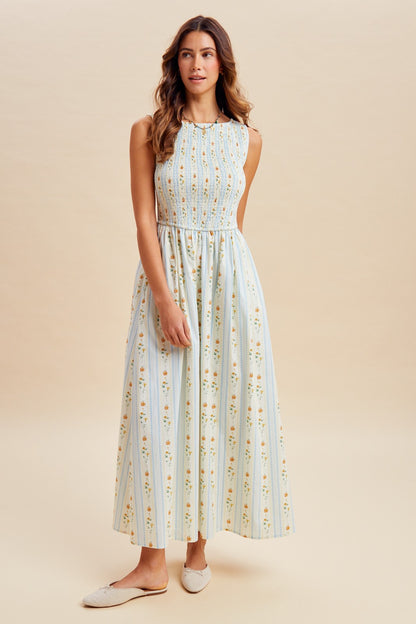 A sleeveless women's high-neck midi dress featuring a fully smocked bodice, convenient side pockets, and an A-line skirt with a vertical blue and orange floral stripe pattern.
