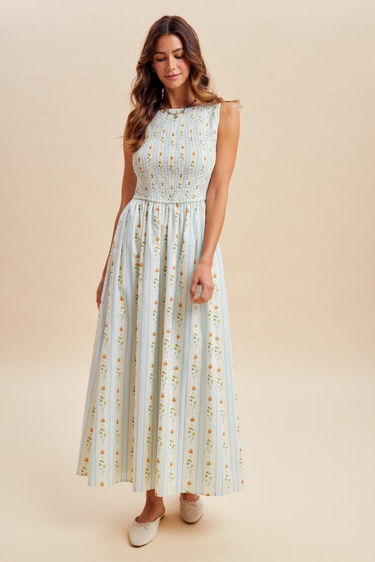 A sleeveless women's high-neck midi dress featuring a fully smocked bodice, convenient side pockets, and an A-line skirt with a vertical blue and orange floral stripe pattern.