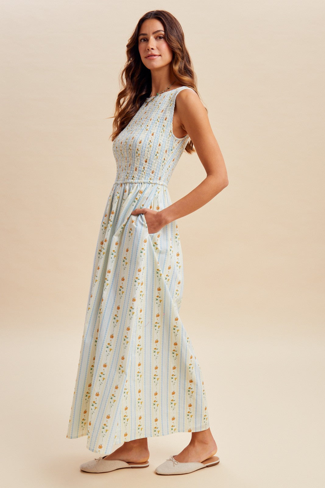 A sleeveless women's high-neck midi dress featuring a fully smocked bodice, convenient side pockets, and an A-line skirt with a vertical blue and orange floral stripe pattern.