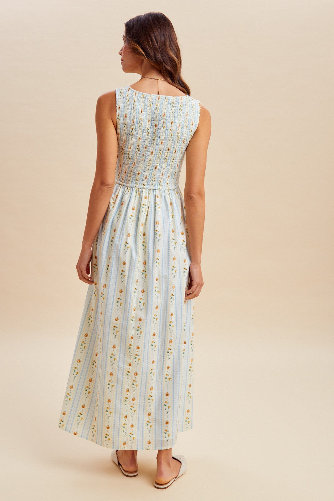 A sleeveless women's high-neck midi dress featuring a fully smocked bodice, convenient side pockets, and an A-line skirt with a vertical blue and orange floral stripe pattern.