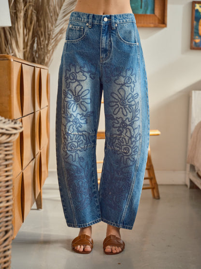 A pair of high-waisted women's barrel jeans in a dark wash featuring intricate tonal blue floral embroidery down the front of the curved legs.