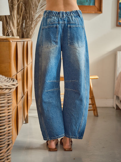 A pair of high-waisted women's barrel jeans in a dark wash featuring intricate tonal blue floral embroidery down the front of the curved legs.
