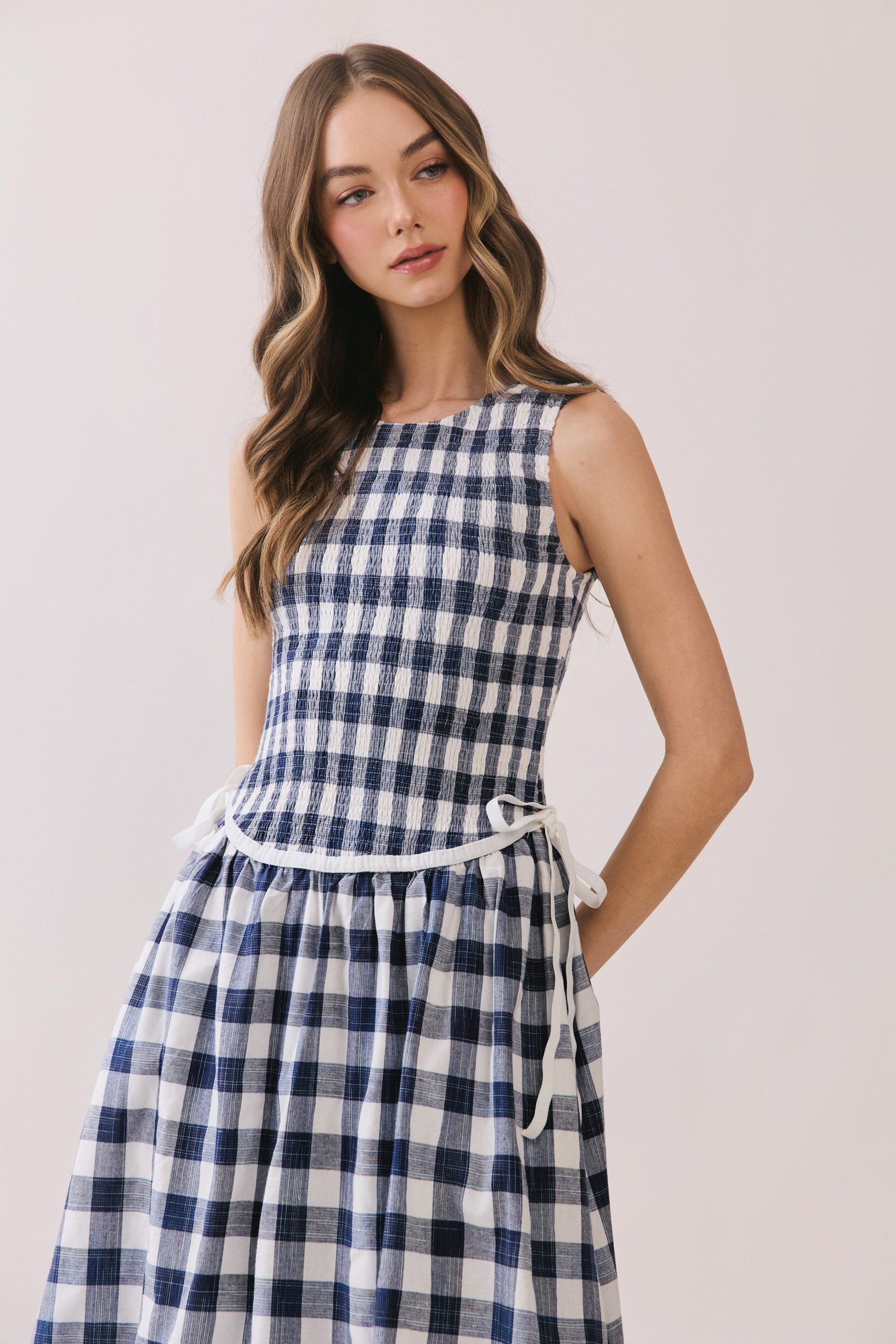 Sleeveless navy and white gingham dress with a smocked bodice and a waist tie detail. 
