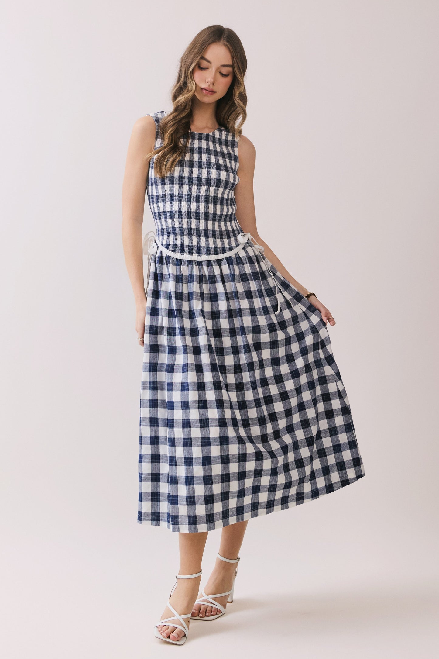 Sleeveless navy and white gingham dress with a smocked bodice and a waist tie detail. 