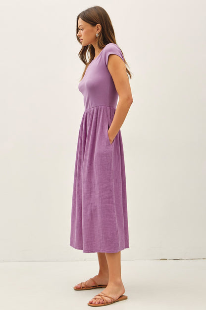 iris purple midi dress featuring a wide boat neckline, short cap sleeves, and a soft gathered waistline with a relaxed flowy skirt.